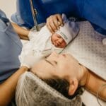 Mama przytulająca noworodka na szpitalnym łóżku po porodzie