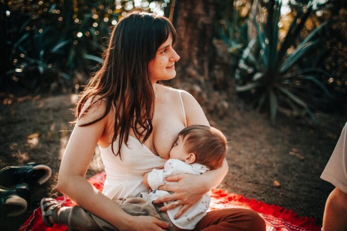 Mama karmiąca piersią niemowlę na kocu na świeżym powietrzu latem